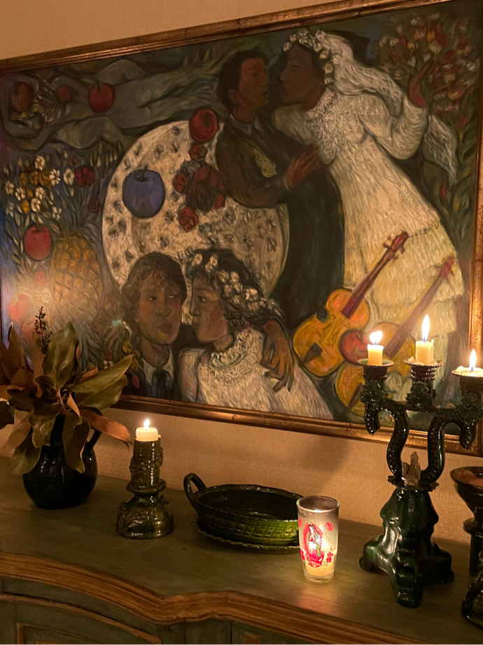 An image of a beautiful painting framed on the wall above a credenza with lit candles.