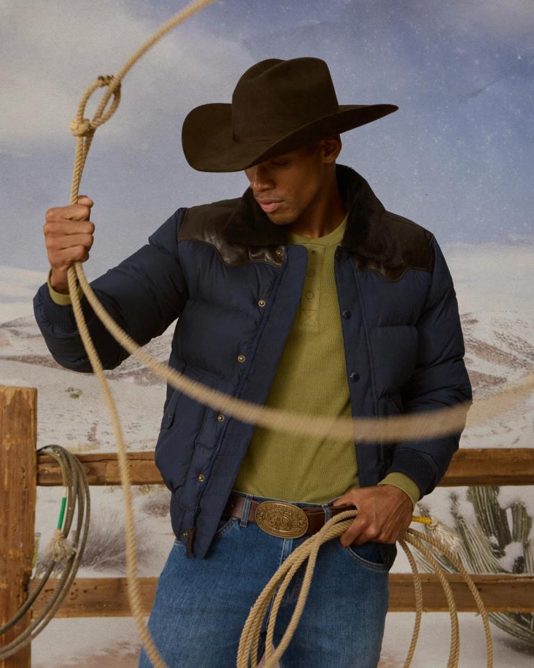 Man in cowboy hat and navy puffer jacket with a lasso.