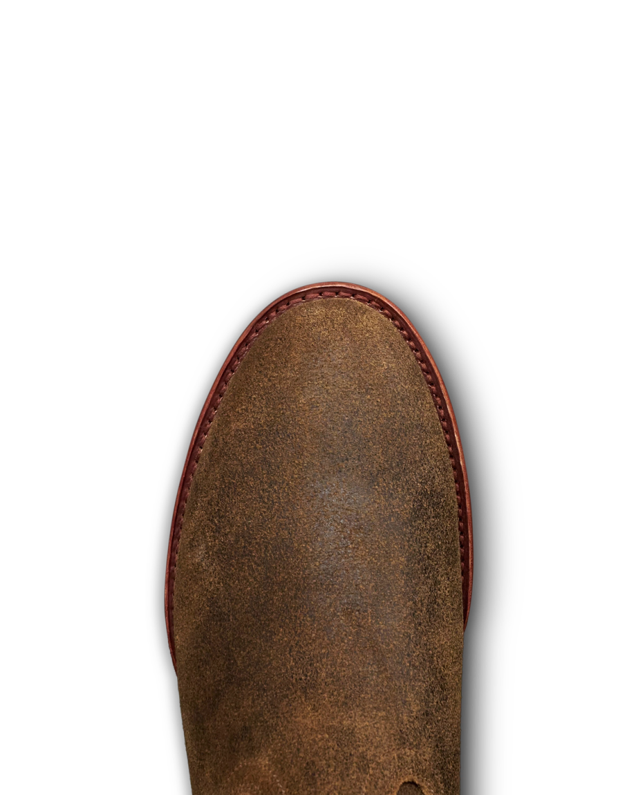 The Glen in Dustwood Roughout. Close-up of the toe area of The Glen Roughout brown suede boot with red stitching along the edge, shown against a white background.