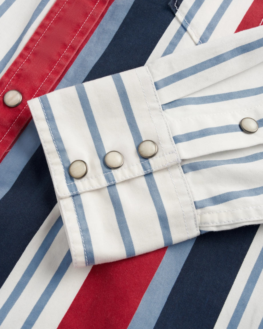 A close-up of a striped shirt cuff with three silver snap buttons. The shirt features vertical blue, white, red, and navy stripes.