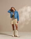 Woman wearing a dress, denim jacket, and white cowgirl boots in a photo studio