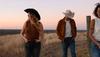 Women and man walking in field wearing cowboy hats and jeans