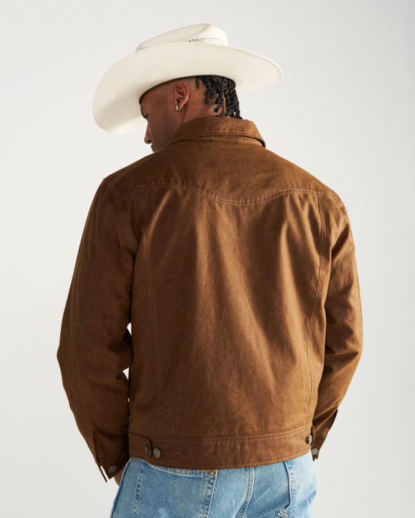 A person seen from behind wearing a white cowboy hat and a brown jacket over blue jeans.