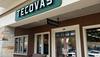 Storefront of Tecovas, featuring a green sign with white lettering above the entrance. A bench is placed outside the store, and the glass doors reveal the interior.