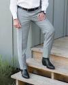 A person in grey dress pants, a white shirt, and black textured dress boots stands with one foot on a wooden step outside a building.