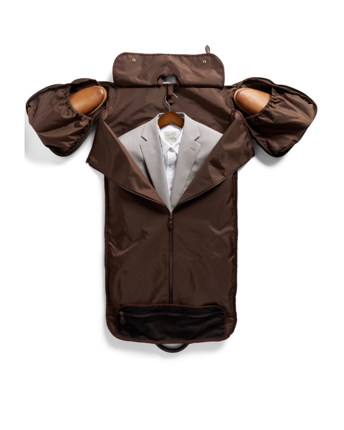 Brown garment bag opened to reveal a gray suit on a hanger, with extended side pockets and a small zippered compartment at the bottom.