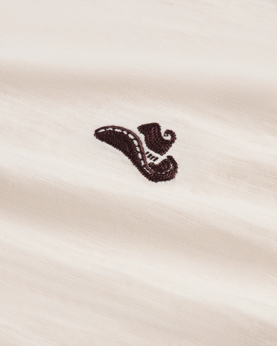 Close-up of a cream-colored fabric with a small, black embroidered design resembling a stylized shoe or horn in the center.