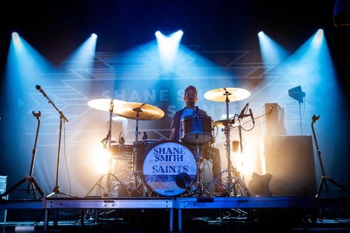 Drummer performing on stage with a vibrant blue light showcasing "shane smith & the saints" on the bass drum.