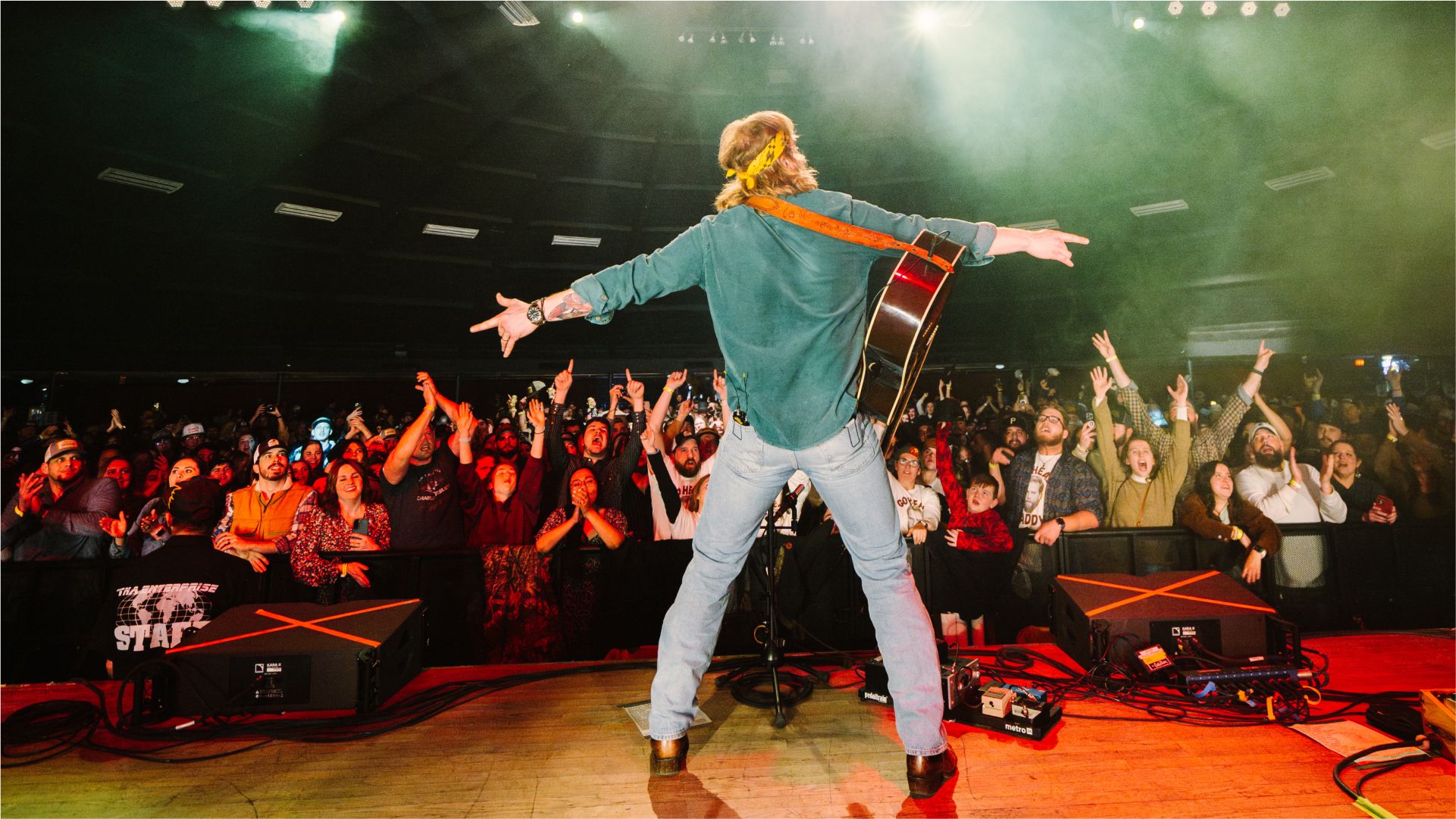 A man performing on stage with guitar in green shirt
