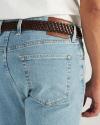 Close-up of a person wearing light blue jeans, a white shirt, and a brown braided leather belt. The jeans have a back pocket and a brown leather brand patch.