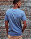 Man wearing the standard issue pocket tee in blue fin in front of a rustic wall