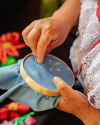 A person hand-embroiders small white stars on blue fabric using an embroidery hoop, surrounded by vibrant floral details.