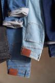 Three denim jackets in black, light blue, and dark blue hang side by side with sleeves rolled up and brown leather patches visible near the hems.