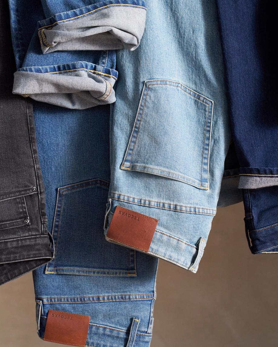 Three denim jackets in black, light blue, and dark blue hang side by side with sleeves rolled up and brown leather patches visible near the hems.