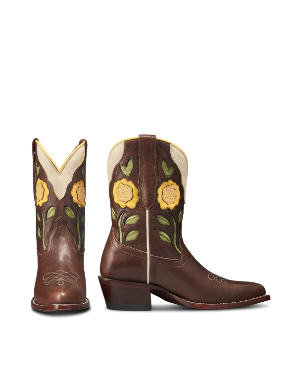 The Jolene in Truffle Cowhide. Brown leather cowboy boots with yellow floral and green leaf appliqués on the shaft, cream leather trim, and a stacked heel—crafted with premium truffle cowhide. Shown from front and side angles.