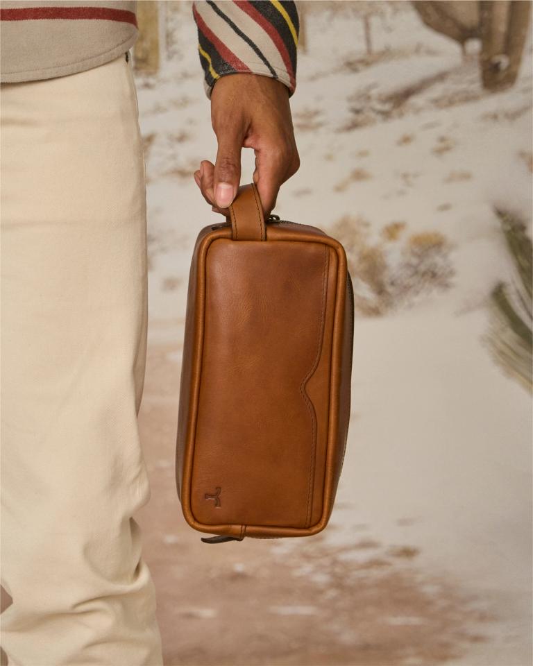 A man holding a travel bag in front of a desert.