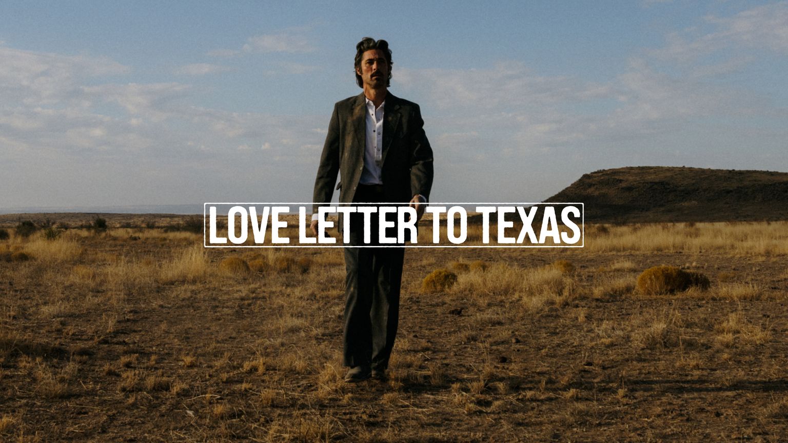 A man in a suit stands in a dry, grassy field under a blue sky with the text "LOVE LETTER TO TEXAS" across the image.