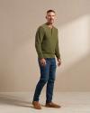 Man wearing jeans and slip ons with a green long sleeve in a photo studio