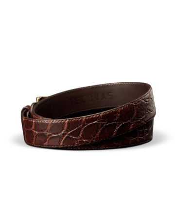 A brown crocodile-embossed leather belt with a gold buckle, coiled on a white background. The brand name “Tecovas” is stamped inside.