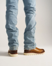 The Knox in Wheat Cowhide. Person wearing light blue jeans and The Knox Cowhide boots with white soles, standing on a white surface, photographed from behind.