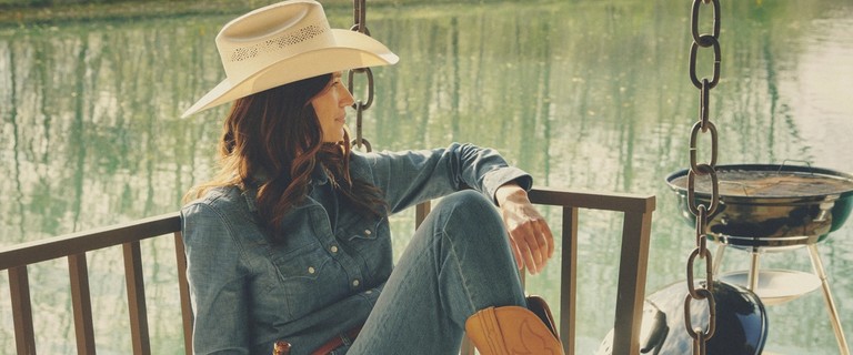 Woman in cowboy hat and cowgirl boots sitting on a swing