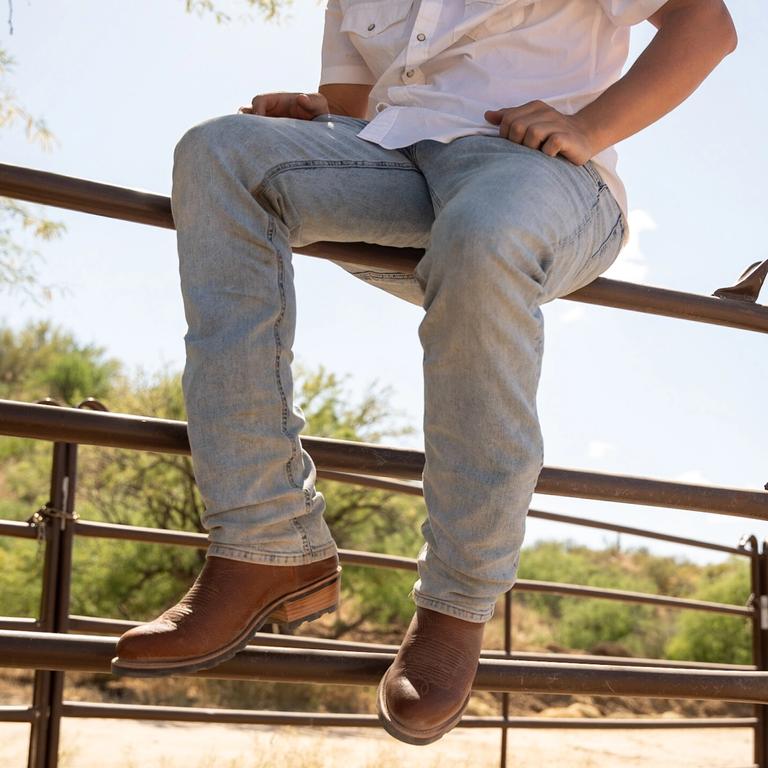 a man on a fence in brown cowboy boots and light wash jeans