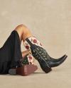Person wearing a black dress and floral embroidered cowboy boots with a light background, showing TECOVAS logo on the sole.