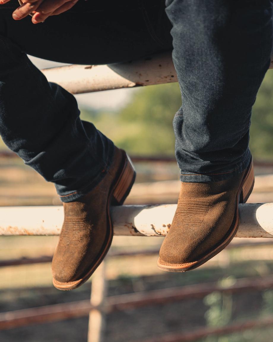 Man wearing Cody Sandstone sitting on a fence at a ranch