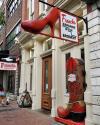 Storefront with a large red high heel sign and oversized red cowboy boot statue outside French's Shoes & Boots; sign reads “French’s Bargains in the Basement.”.