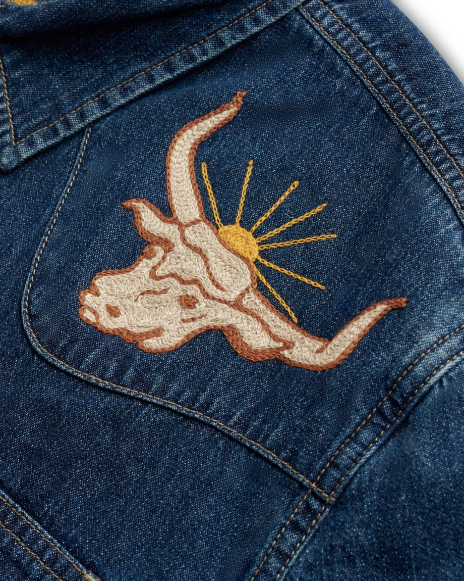 Denim jacket with embroidered bull skull and sunburst design on the back.