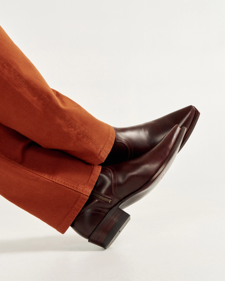 Person wearing brown dress shoes and orange pants, with legs crossed against a plain background.