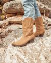 A person wearing blue jeans and light brown cowboy boots standing on a rocky surface outdoors.