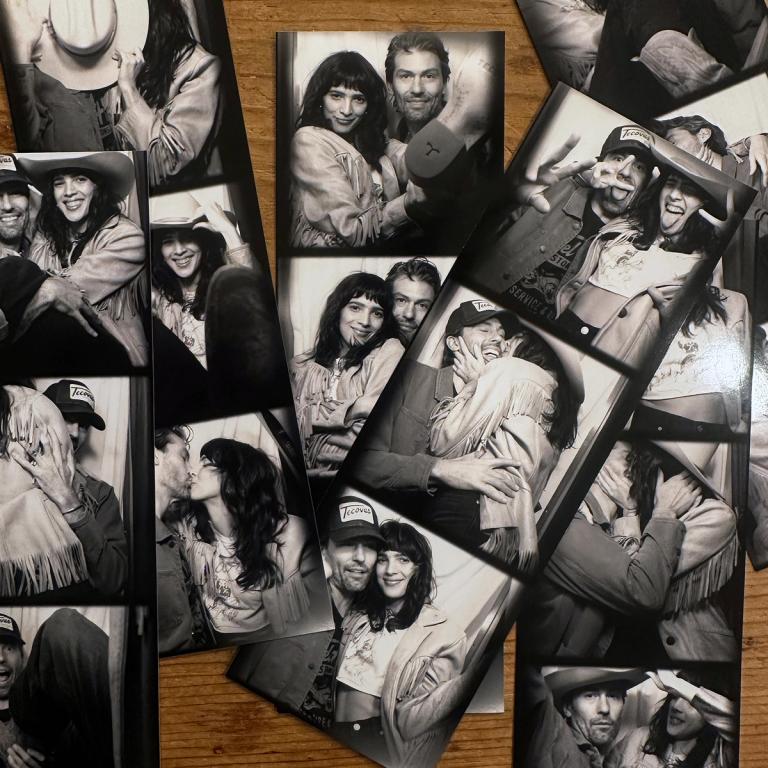 Several black-and-white photo booth strips of a smiling couple posing together, arranged on a wooden surface.