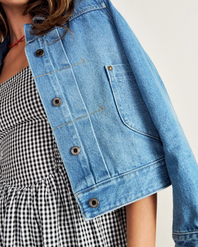 A person wearing a blue denim jacket over a black and white gingham dress, shown from the shoulders to the waist.