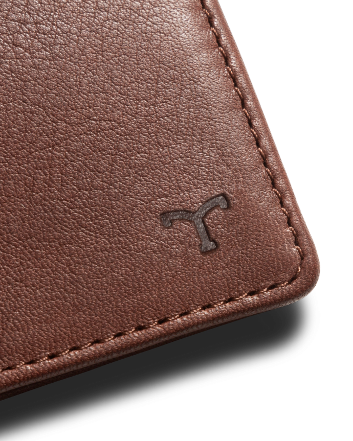 Close-up of a brown leather material with visible stitching and a small embossed logo in the corner.