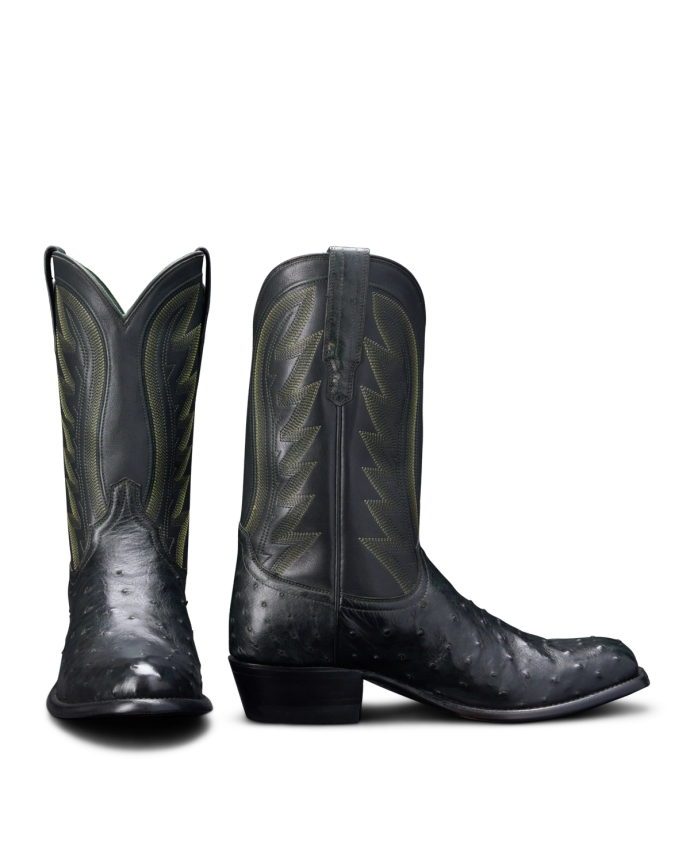 A pair of black cowboy boots with green stitching and decorative patterns, shown against a black background.