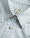 Close-up of a light blue shirt collar with visible stitching. It features two buttons and a label that reads "Tecovas, Designed in Austin, Texas, Made in Thailand.