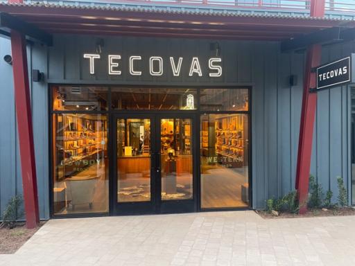 Storefront of Tecovas, featuring large illuminated signage, glass doors, and displays of cowboy boots inside.