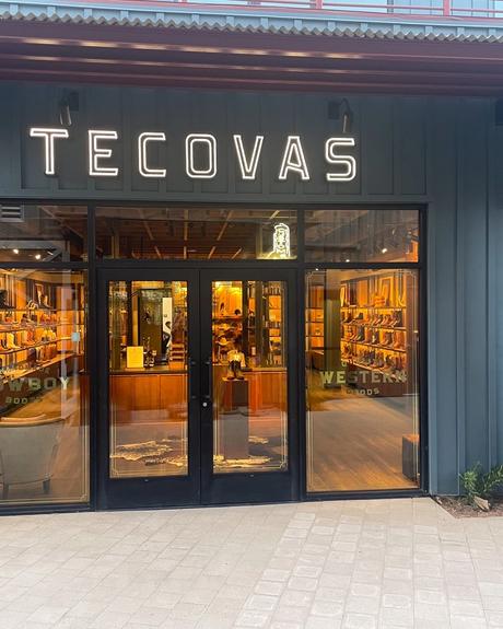 Storefront of Tecovas, featuring large illuminated signage, glass doors, and displays of cowboy boots inside.