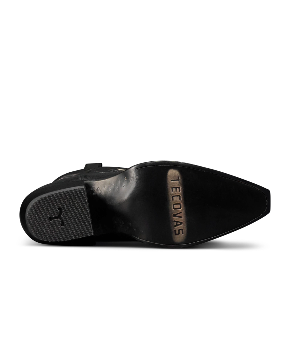 The Annie in Midnight Cowhide. The underside of a Midnight Cowhide black dress shoe showing a pointed toe, textured heel, and the brand name "Tecovas" engraved on the sole.