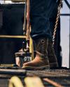 Close-up of a person wearing cowboy boots and jeans standing on a metal surface, surrounded by tools and equipment.