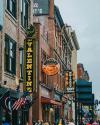 Lively street scene on nashville's broadway featuring neon signs, including ones for "valentin hotel" and "whiskey bent saloon," with a bustling crowd and historic buildings.