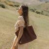 Woman in a field carrying a leather tote bag