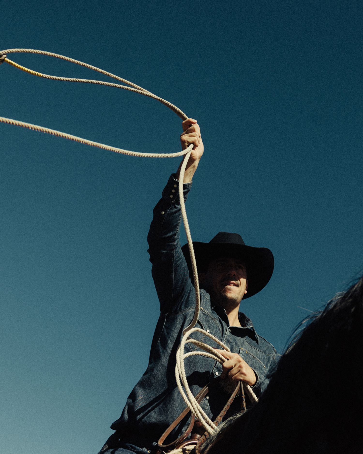 White cowboy hat with decorative engravings, including mountains, a sun, a moon, and cacti, placed on a wooden surface with an abstract painting in the background.