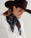 A person wearing a dark brown cowboy hat, white button-up shirt, and a navy blue patterned scarf tied around their neck.