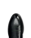 Top view of a shiny black leather shoe with green decorative stitching on the toe, set against a black background.