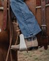 Close-up of a person wearing jeans and boots in a stirrup while sitting on a horse saddle.