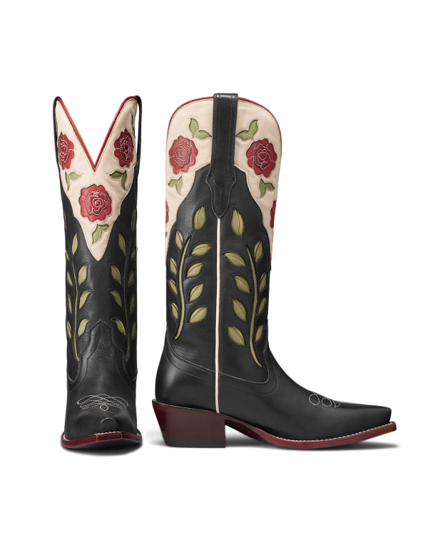 The Annie in Midnight Roses Cowhide. A pair of black cowhide cowboy boots with green leaf and red rose embroidery, cream and red trim, pointed toes, and angled heels—these Midnight Roses Cowhide boots blend classic Western style with striking floral details.