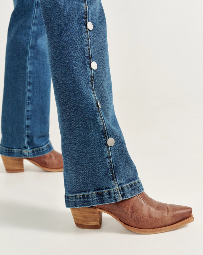 Close-up of a person wearing blue jeans with side buttons and brown leather cowboy boots.