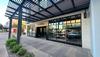 Exterior of a Tecovas store with large windows and a black metal awning, showing parked cars reflected in the glass and landscaped sidewalk in front.